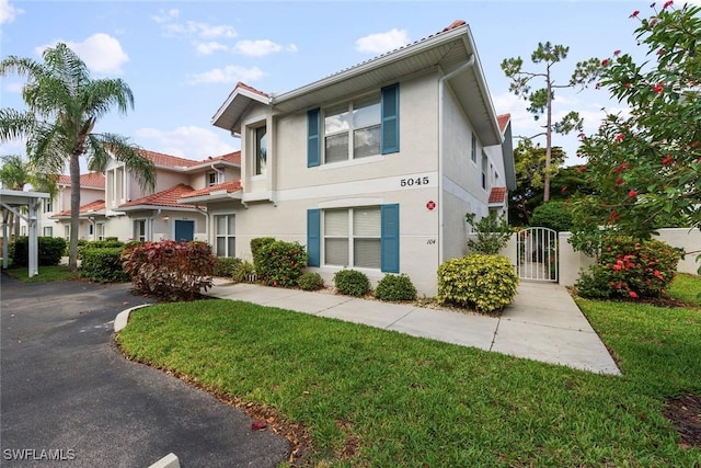 5045 Cedar Springs Dr Unit 104, Naples, FL 34110 - view of front facade with a gate, a front lawn, a tile roof, and stucco siding