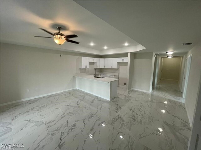 1111/1113 Circle Dr, Lehigh Acres, FL 33973 - kitchen with a peninsula, a sink, baseboards, a tray ceiling, and white cabinetry