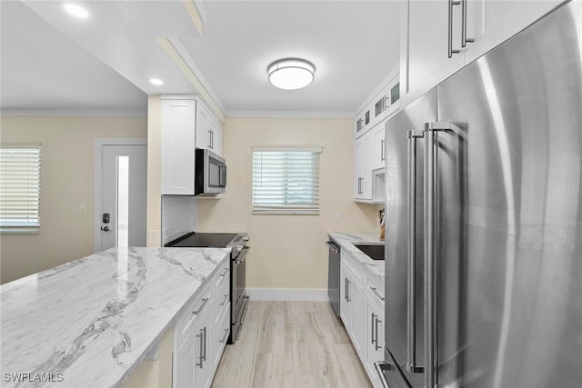kitchen featuring white cabinets, stainless steel appliances, light stone countertops, and crown molding