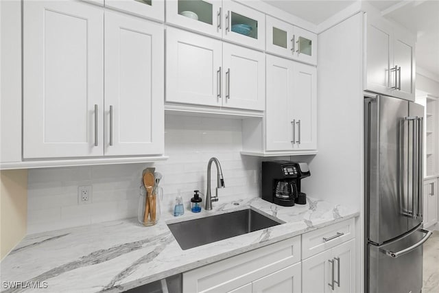 kitchen with white cabinets, a sink, high end refrigerator, decorative backsplash, and glass insert cabinets
