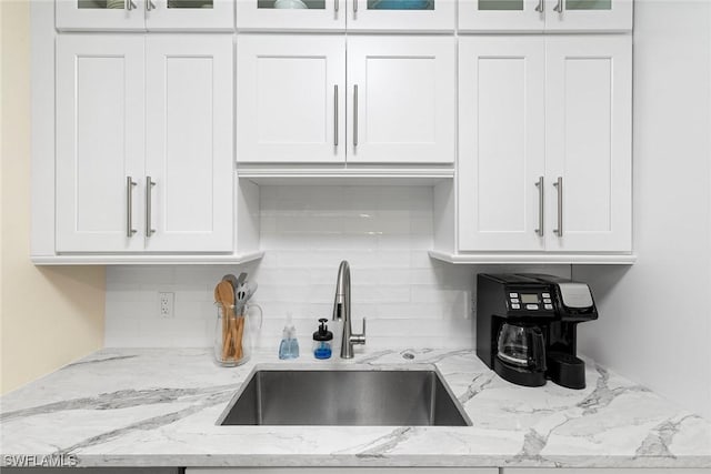 kitchen with white cabinets, glass insert cabinets, a sink, and tasteful backsplash