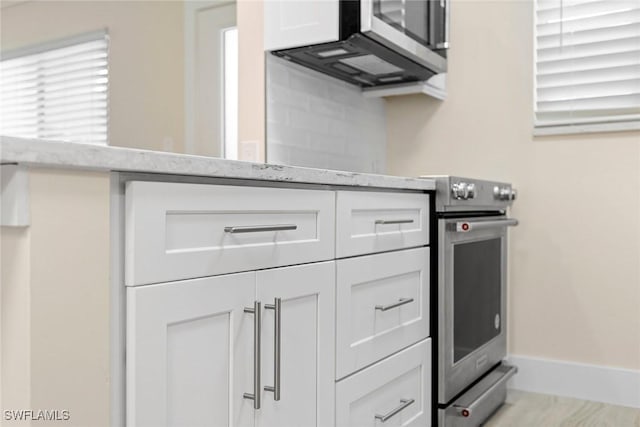 kitchen with light stone countertops, backsplash, white cabinetry, and electric stove