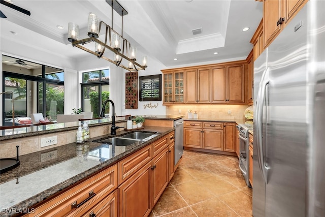 7996 Cordoba Pl, Naples, FL 34113 - kitchen with stainless steel appliances, a sink, a raised ceiling, brown cabinets, and tasteful backsplash