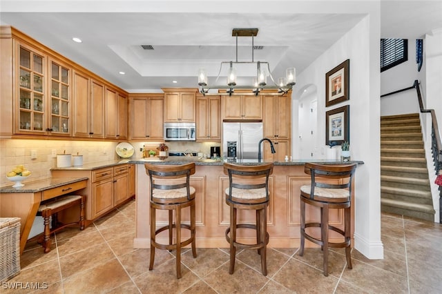7996 Cordoba Pl, Naples, FL 34113 - kitchen with stainless steel appliances, a raised ceiling, a breakfast bar area, glass insert cabinets, and backsplash