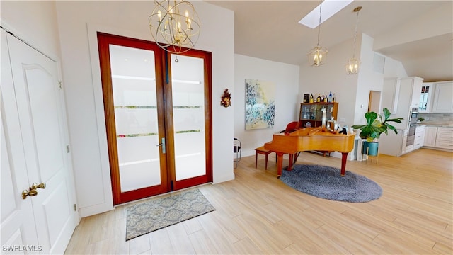 entrance foyer with a chandelier, light wood-style flooring, french doors, vaulted ceiling, and a skylight
