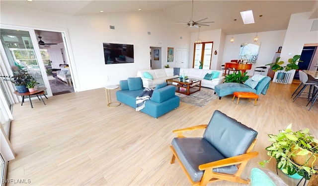 living room with a ceiling fan, wood finished floors, high vaulted ceiling, and a skylight