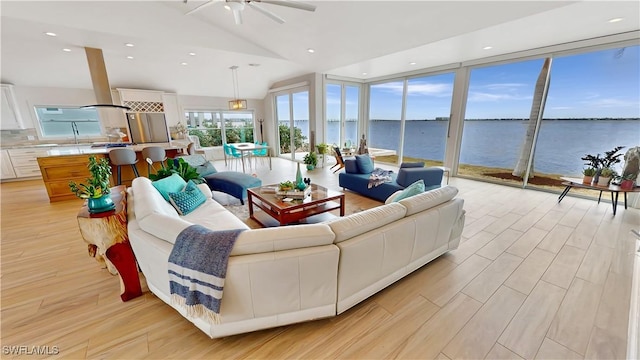 living area with ceiling fan, vaulted ceiling, a water view, light wood-style flooring, and recessed lighting