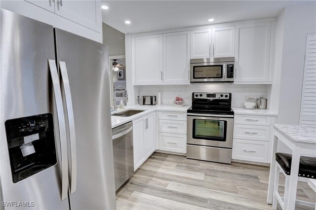 kitchen with tasteful backsplash, a sink, light countertops, white cabinets, and appliances with stainless steel finishes