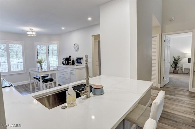 kitchen featuring baseboards, recessed lighting, white cabinetry, wood finished floors, and a breakfast bar