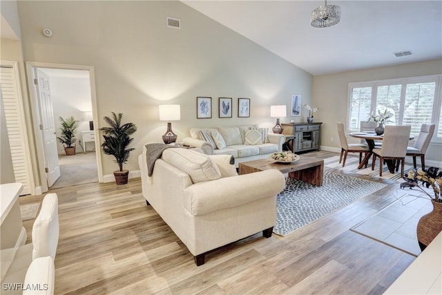 living room with high vaulted ceiling, baseboards, visible vents, and light wood-type flooring