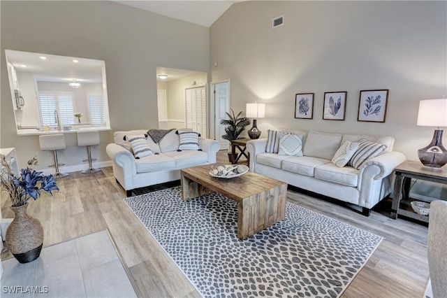 living room featuring lofted ceiling, wood finished floors, visible vents, and baseboards