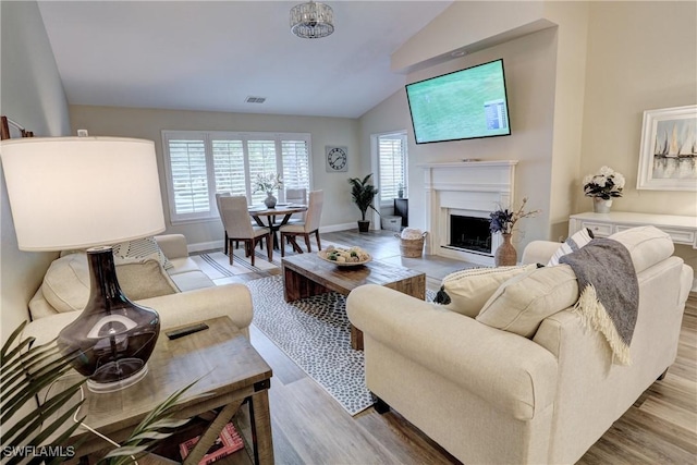 living area with light wood finished floors, vaulted ceiling, baseboards, visible vents, and a fireplace
