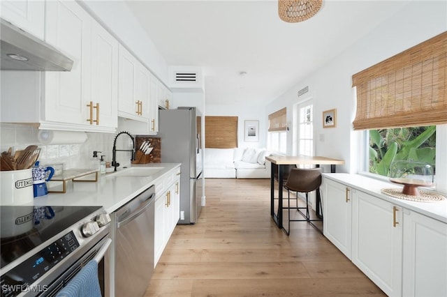 kitchen with a sink, stainless steel appliances, light wood finished floors, white cabinets, and visible vents