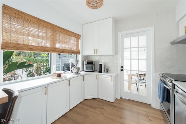 kitchen with white cabinets, backsplash, appliances with stainless steel finishes, and light wood-style floors
