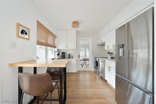 kitchen featuring stainless steel fridge, light wood-style flooring, white cabinets, backsplash, and under cabinet range hood