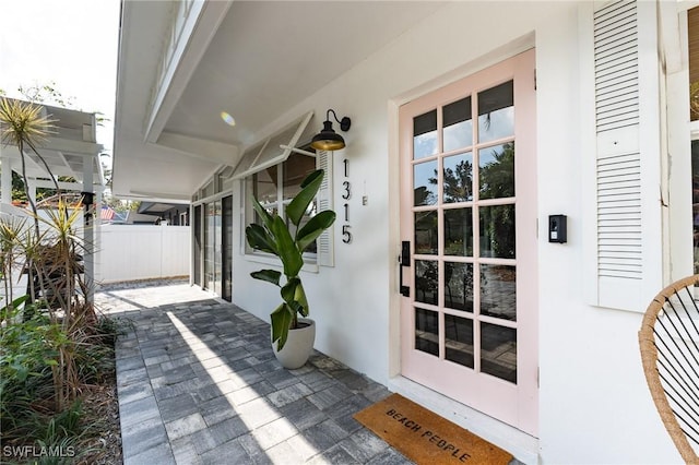 entrance to property with stucco siding, fence, and covered porch