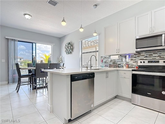 kitchen with stainless steel appliances, a peninsula, a sink, visible vents, and light countertops