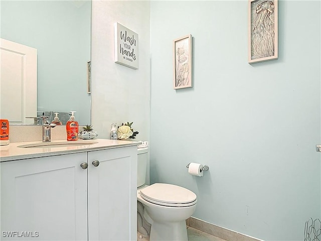 half bath with baseboards, vanity, and toilet