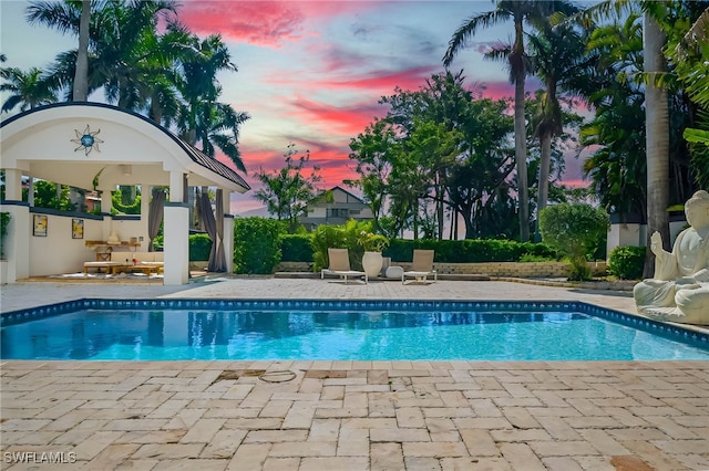 pool at dusk with a patio area, a gazebo, and an outdoor pool