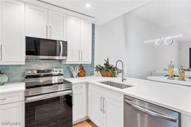 kitchen with decorative backsplash, stainless steel appliances, light countertops, a sink, and white cabinetry