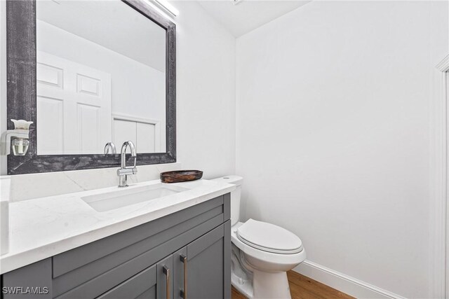 bathroom with toilet, wood finished floors, vanity, and baseboards