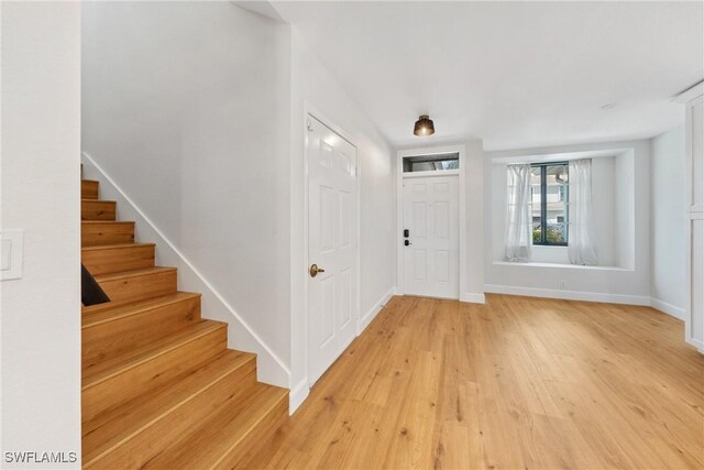 entryway with baseboards, stairs, and light wood finished floors