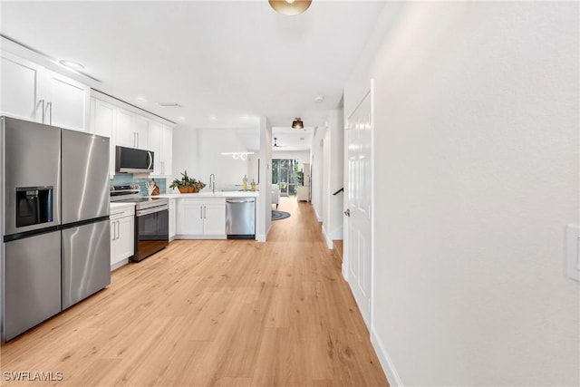 kitchen with appliances with stainless steel finishes, white cabinetry, light countertops, and light wood finished floors