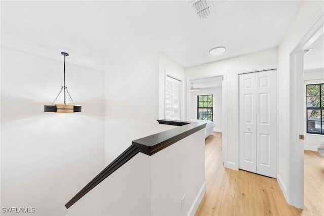 hall with an upstairs landing, visible vents, baseboards, and light wood-type flooring