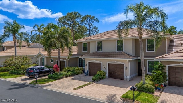 mediterranean / spanish-style home with driveway, an attached garage, a tiled roof, and stucco siding