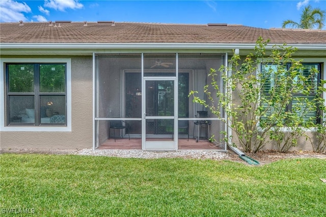 rear view of property featuring a lawn, stucco siding, and a sunroom