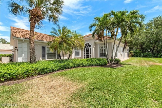 mediterranean / spanish house featuring stucco siding, a tiled roof, and a front yard