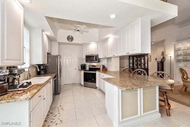 kitchen featuring a breakfast bar area, appliances with stainless steel finishes, a sink, a ceiling fan, and a peninsula