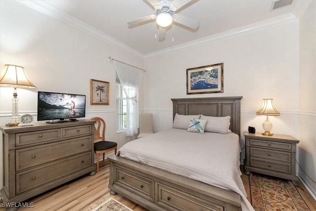 bedroom with crown molding, a wainscoted wall, visible vents, and light wood-type flooring