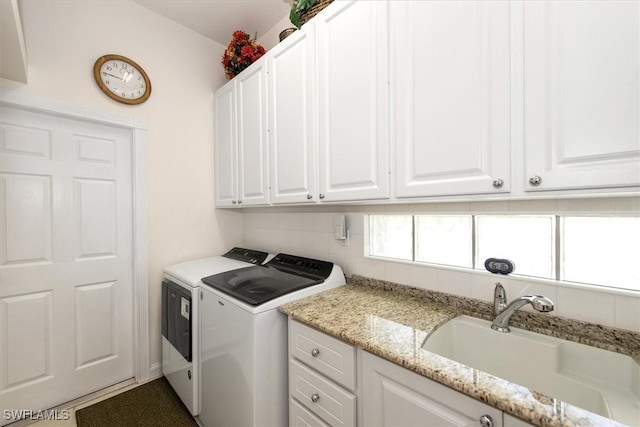 clothes washing area featuring washing machine and dryer, cabinet space, and a sink