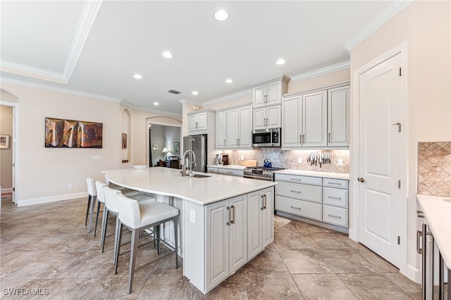 kitchen with decorative backsplash, a breakfast bar area, arched walkways, stainless steel appliances, and a center island with sink