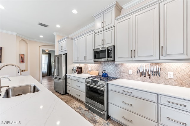kitchen with a sink, visible vents, backsplash, appliances with stainless steel finishes, and ornamental molding