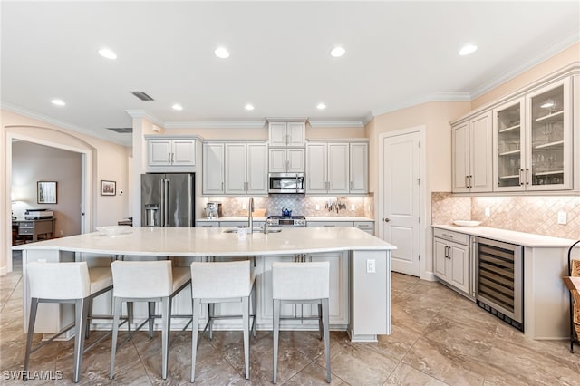 kitchen with stainless steel appliances, wine cooler, visible vents, a sink, and a center island with sink