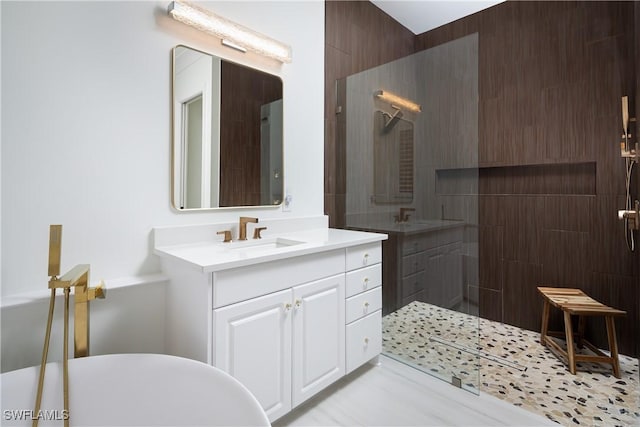 bathroom featuring a walk in shower, two vanities, a freestanding bath, and a sink