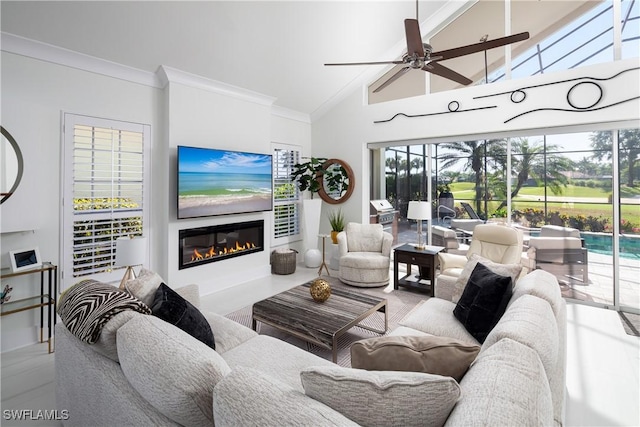 living room with a glass covered fireplace, a ceiling fan, ornamental molding, and high vaulted ceiling