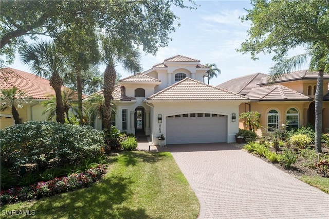 mediterranean / spanish home with a tile roof, decorative driveway, stucco siding, a front lawn, and a garage