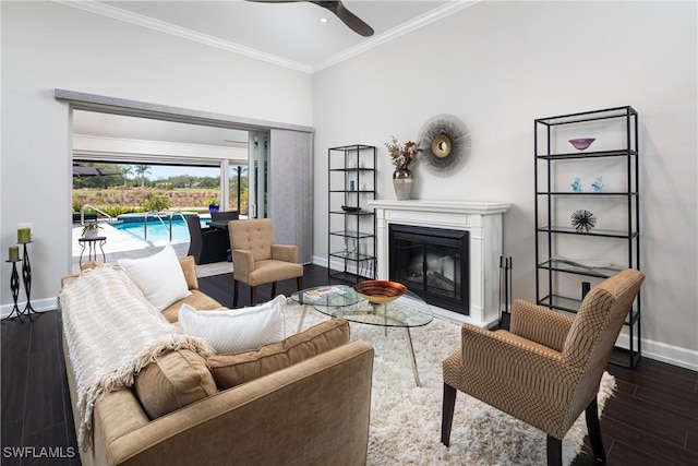 living area featuring dark wood-type flooring, a glass covered fireplace, a ceiling fan, baseboards, and ornamental molding