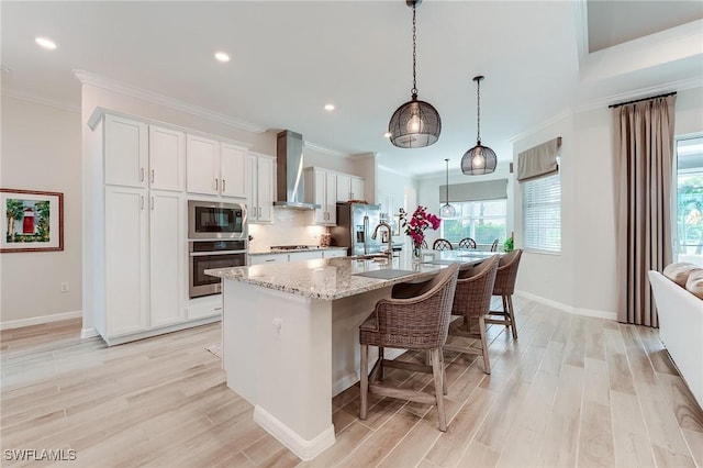 15951 Talon Ter, Punta Gorda, FL 33982 - kitchen featuring wall chimney range hood, a kitchen bar, appliances with stainless steel finishes, a center island with sink, and light wood-type flooring
