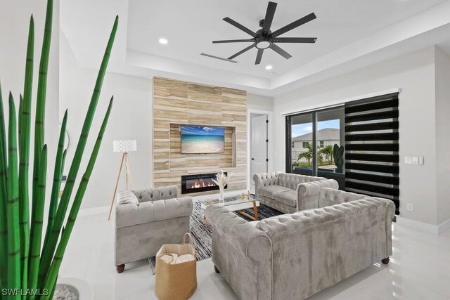 living room featuring a raised ceiling, a ceiling fan, recessed lighting, a fireplace, and baseboards