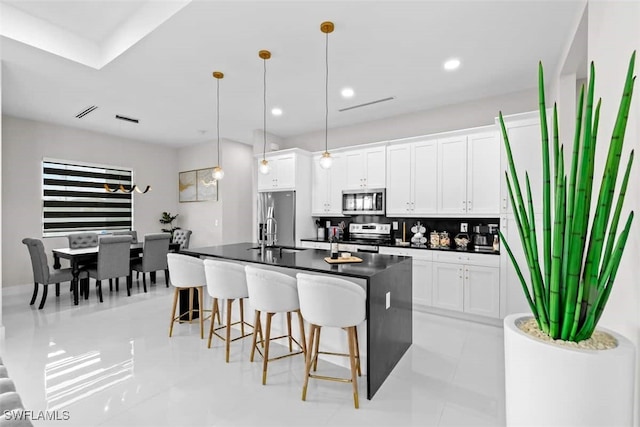 kitchen with appliances with stainless steel finishes, dark countertops, a kitchen bar, white cabinetry, and recessed lighting