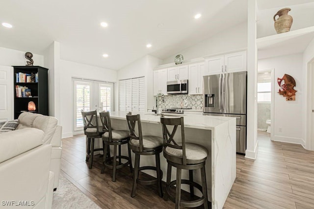 kitchen featuring a breakfast bar area, appliances with stainless steel finishes, an island with sink, and vaulted ceiling