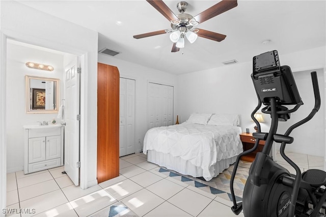 bedroom featuring light tile patterned flooring, visible vents, ceiling fan, and two closets