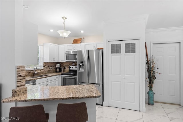 kitchen with light stone counters, white cabinets, a sink, appliances with stainless steel finishes, and a peninsula
