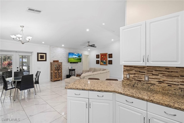 kitchen with light stone countertops, a peninsula, backsplash, white cabinets, and french doors