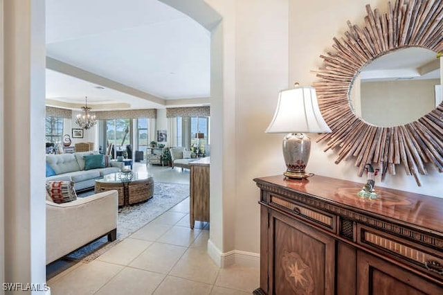 hallway with light tile patterned flooring, a chandelier, a tray ceiling, baseboards, and ornamental molding