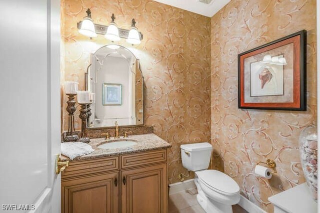 bathroom featuring tile patterned floors, wallpapered walls, vanity, baseboards, and toilet